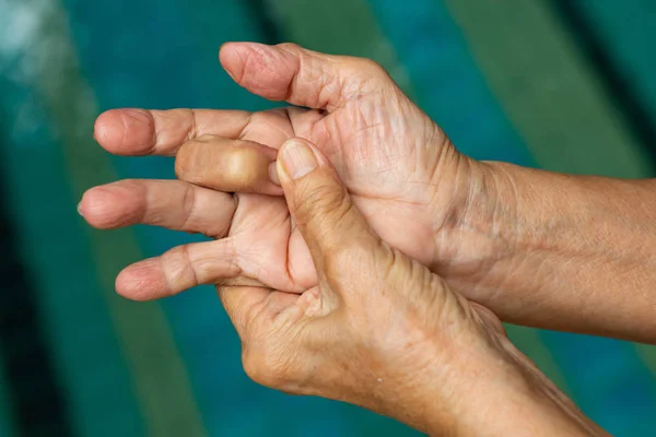 Trigger Finger, Senior woman's left hand massaging her middle finger, Suffering from pain, Close up and macro shot, Swimming pool background, Health care and massage, asian body concept — Stock Photo, Image