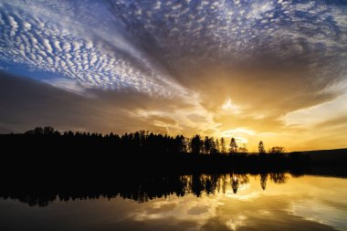 Turuncu ve mavi dramatik bulutlar ile gün batımı ve Vrbov gölün su yüzeyinde yansıması, Slovakya.