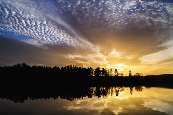 Turuncu ve mavi dramatik bulutlar ile gün batımı ve Vrbov gölün su yüzeyinde yansıması, Slovakya.
