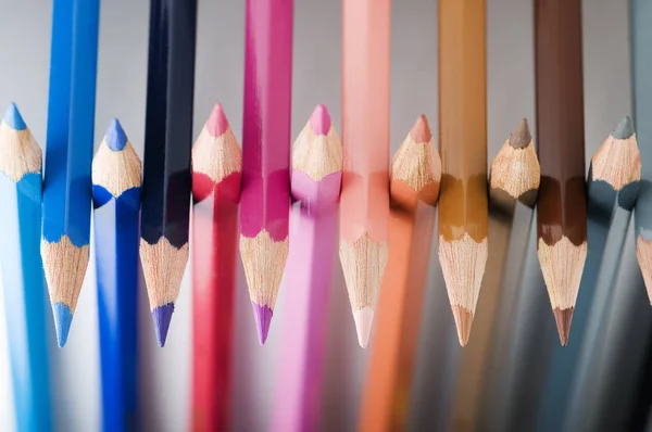 Tarafsız gri bir arkaplanda yan yana dizilmiş renkli kalem uçlarının yakın plan görüntüsü.