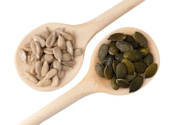 Güneş çekirdeği ve balkabağı tohumlarıyla dolu iki tahta kaşığın yakın çekim görüntüsü beyaz üzerine izole edilmiş.