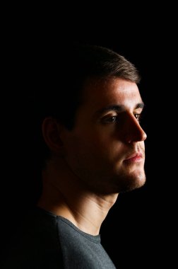 Sağdan siyah arka planda parlayan ışığa bakan genç bir adamın yan baş portresi..