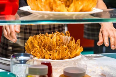 Kızarmış soğan kızartmasının yakın plan resmi. Yiyecek standında servis edilen beyaz tabakta. Altın aperatif taze hazırlandı ve soslar ve baharatlarla çevrili olarak yenmeye hazır. Sokak yemekleri, abur cuburlar, fast food ve gastronomi konuları için mükemmel bir tema.