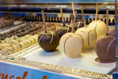 Çikolata kaplı elmalar, şekerleme dükkanında sergileniyor. Elmalar sütle, sütle ve dekoratif çiselemeli koyu çikolatayla kaplanarak, fuarlarda, karnavallarda ve açık hava pazarlarında sıkça rastlanan popüler bir tatlı ziyafeti yaratıyor..