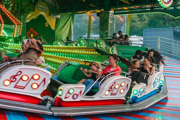 Eğlence fuarında Music Express 'e binen ziyaretçiler. Renkli ışıklar ve hızlı hareketlerle aydınlatılmış yolculuk heyecan, aile eğlencesi ve geleneksel fuar alanı eğlencesini gösteren canlı bir karnaval atmosferi yaratıyor.