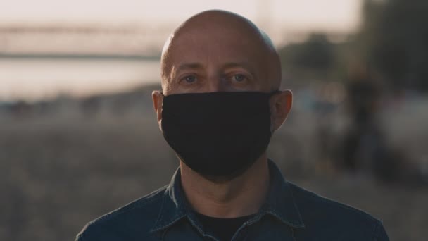 Face of mid-forties bald man on the beach during the amazing sunset who is wearing a black cloth mask. — Stock Video