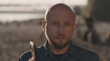 Kırklı yaşlarının ortasında, şık sakallı kel bir adam güzel bir günbatımında sahilde dikiliyor. O, telefonda biriyle ciddi bir konuşma yapıyor. Endişeli..