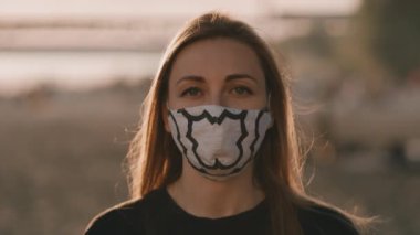 Gün batımında plajda maske takan genç bir kadının yüzü..