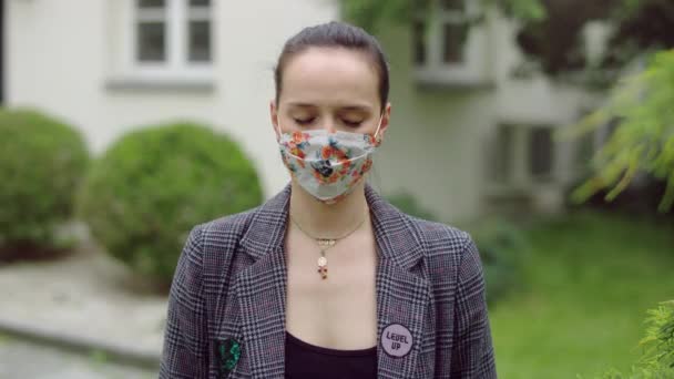 Young woman wearing cloth colorfull mask with her eyes closed is standing in the garden. — Stock Video