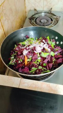 Vertical 1080x1920 footage of red amaranth (lal shak) in a wok on a gas stove. Onion, green chili and salt are added and tossed in a home style kitchenclean, appetizing preparation; no people.