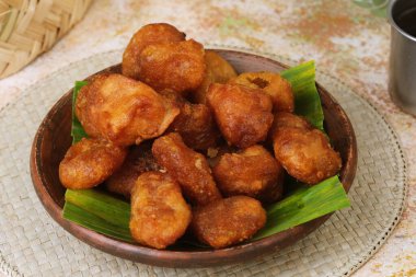 Fried cassava snack Getuk Goreng, golden brown fritters served on rustic plate with banana leaf decoration.