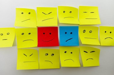 Mutlu bir kırmızı ve üzgün bir mavi de dahil olmak üzere çeşitli çizilmiş yüzlere sahip bir grup yapışkan nota, farklı ifadelere sahip sarı notalar arasında sıralanır..