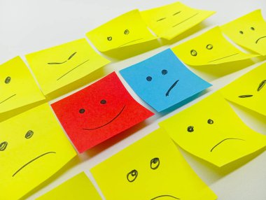 Mutlu bir kırmızı ve üzgün bir mavi de dahil olmak üzere çeşitli çizilmiş yüzlere sahip bir grup yapışkan nota, farklı ifadelere sahip sarı notalar arasında sıralanır..