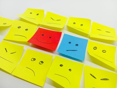 Mutlu bir kırmızı ve üzgün bir mavi de dahil olmak üzere çeşitli çizilmiş yüzlere sahip bir grup yapışkan nota, farklı ifadelere sahip sarı notalar arasında sıralanır..