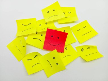 Mutlu yüzlü tek bir kırmızı yapışkan not hüzünlü veya nötr yüzlü, bireyselliği ve olumlu bir görünümü sembolize eden sarı yapışkan notlar yığınından çıkar..