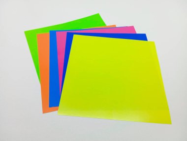 Açık gri bir yüzey üzerinde köşegen şeklinde yayılmış birkaç parlak neon renkli kağıt yığınının hava görüntüsü..