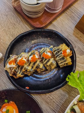 Ön manzara leziz ve lezzetli. Siyah bir tabakta balık yumurtası ve mayonezden oluşan lezzetli kızarmış suşi ruloları..