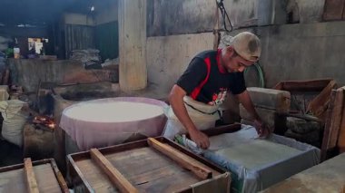 Kediri, Endonezya 13 Haziran 2024 video görüntüleri bir tofu fabrikası işçisi geleneksel bir Kediri fabrikasında büyük fıçıların yanında taze tofu hazırlıyor ve şekillendiriyor..