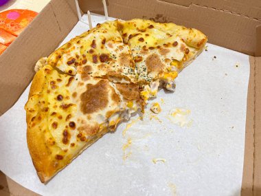 Kısmen yenmiş altın hamurlu peynirli pizza ve karton bir teslimat kutusunun içinde eritilmiş sos, lezzetli fast food yemeği..