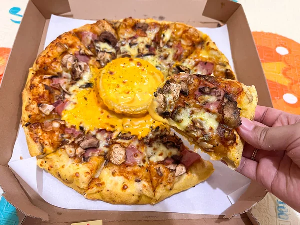 Yakın plan çekimde mantarlı, jambonlu ve erimiş peynirli bir dilim pizza karton bir teslimat kutusunda servis edilen taze fırında pizza..