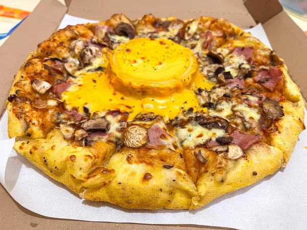 Mantarlı, jambonlu, mozarellalı ve ortasında erimiş peynir soslu lezzetli pizza karton bir teslimat kutusunda sıcak servis ediliyor..