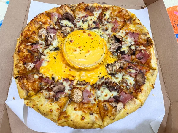 Mantarlı, jambonlu, mozarellalı ve ortasında erimiş peynir soslu lezzetli pizza karton bir teslimat kutusunda sıcak servis ediliyor..