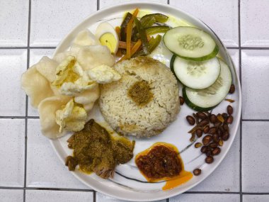Beyaz tabakta sambal, sebze, fıstık ve çıtır kraker bulunan geleneksel Endonezya pirinç tabağı, yemek menüleri ve mutfak promosyonları için renkli ve iştah açıcı bir sunum yaratıyor..