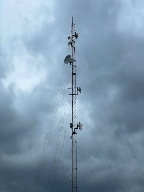 Antenleri ve uydu anteni olan uzun bir iletişim kulesi dengesiz, bulutlu bir gökyüzüne karşı duruyor. Teknoloji ve iletişim temaları için dramatik ve endüstriyel bir atmosfer yaratıyor..