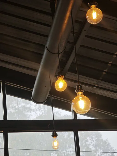 Warm glowing hanging light bulbs in a modern industrial interior with metal ceiling and large windows