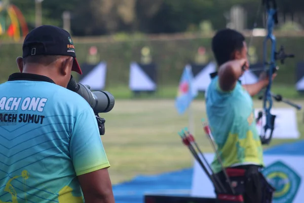 Banda Aceh, Indonesia - September 19, 2025: The coach uses a spotting scope to check accuracy, while the archer is in full draw position with a modern compound bow