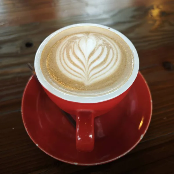 Close-up of a beautifully crafted cappuccino with heart-shaped latte art in a vibrant red cup and saucer, placed on a rustic wooden table