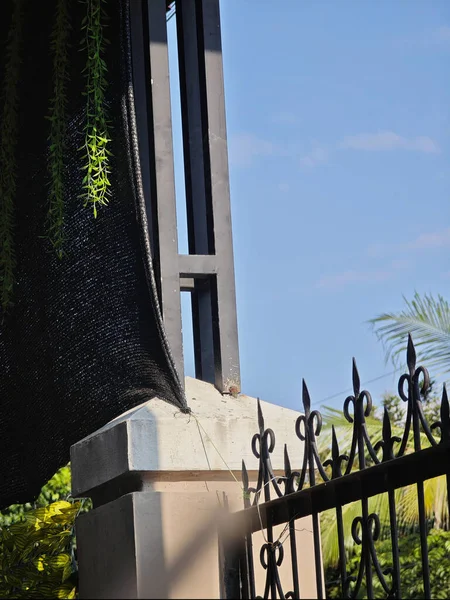 Siyah işlemeli demir kapı ve parlak güneş ışığı altında dikey çerçeveli beton sütun.