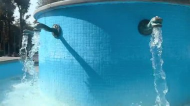 Heykeltraş edilmiş bronzdan akan suyun canlı mavi fayanslı bir yüzeye hayvan başlarını andırdığı dekoratif bir çeşmenin sanatsal görüntüleri. Tazelik, tasarım ve Akdeniz cazibesinin sembolü.