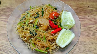 Köftelerle, sebzelerle, domateslerle servis edilen ve ahşap bir masada salatalık ve biberle süslenmiş bir tabak pirinç vermicelli..