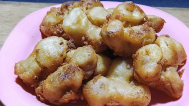 Pembe bir tabakta altın sarısı kızarmış muzlu börek. Ev yapımı tatlı abur cubur, geleneksel Endonezya mutfağı..