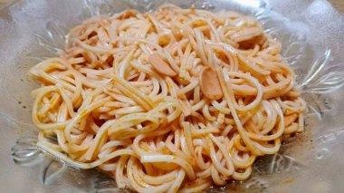 Hafif soslu soslu soslu spagetti eriştesinin yakın çekim, yukarıdan aşağı görüntüsü. Makarna cam bir kasede servis ediliyor. Karışık erişte ve malzemelerin dokusunu gösteriyor..