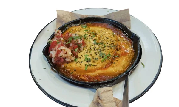 Close up of a cheesy tomato base pizza served in a black skillet on a white plate, garnished with fresh herbs and topped with tomato salsa.