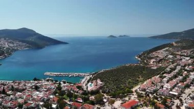 Flight of a drone over the coastal town of Kalkan, Mugla, Turkey. Panoramic view of the city buildings, waterfront, turquoise sea, and islands.60fps