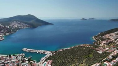 Flight of a drone over the coastal town of Kalkan, Mugla, Turkey. Panoramic view of the city buildings, waterfront, turquoise sea, and islands.60fps