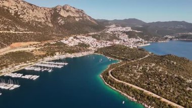 A stunning aerial view of the coastal town of Ka in Turkey. Drone shots showcase the crystal-clear turquoise sea, yachts in the harbor, picturesque mountains, and the charming streets of the town.