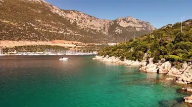 A stunning aerial view of the coastal town of Ka in Turkey. Drone shots showcase the crystal-clear turquoise sea, yachts in the harbor, picturesque mountains, and the charming streets of the town.