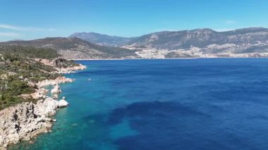 TurquoisAerial panorama of the Mediterranean Sea along the coast of Kalkan, Turkey. Vibrant blue waters, rocky shores, and mountains on the horizon create a picturesque landscape. Perfect for travel, summer vacation, ecotourism, and Turkish Riviera