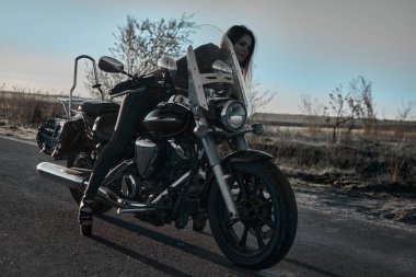 Bir sonbahar tarlasının arka planında güçlü bir motosikletle gezen şık genç bir kadın, özgürlük, macera ve bireysel stil duygusu aktarıyor..