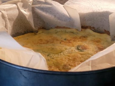 Parşömen kağıdıyla kaplanmış, fırından yeni çıkmış ev yapımı bir omletin yakın çekimi. Omlet servis edilmeye hazır. Görüntü ev yemeklerinin sıcaklığını çağrıştırıyor..