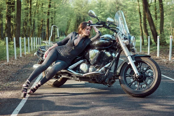 Tulum giymiş güzel bir kadın ve yüksek topuklu ayakkabılar açık havada motosiklet üstünde poz veriyor. Özgürlük ve macera ruhunu kucaklarken kendine güven ve cazibe yayıyor..