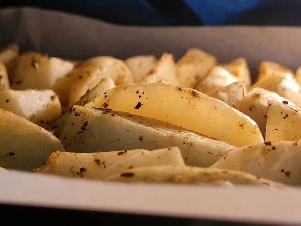 Yakın plan bir resim, parşömen kağıdında fırında pişen baharatlı patates dilimlerini gösteriyor. Altın rengi ve şifalı otlar, yemek temaları için uygun olan mutfak cazibesini vurgular..