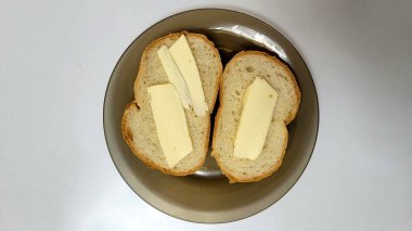 Kahverengi bir tabakta tereyağlı iki parça ekmek, yukarıdan çekilmiş, tereyağı ve ekmek dokusuna odaklanmış basit bir aperatif ya da kahvaltıyı gösteriyor.. 