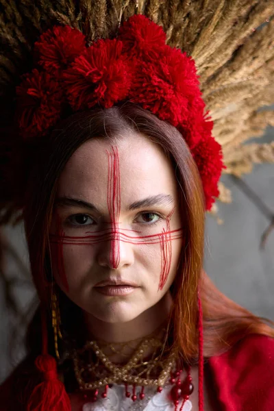 Kırmızı yüz boyası ve geleneksel başlığıyla esrarengiz kadın çarpıcı ve kültürel açıdan zengin bir portre yaratıyor.. 