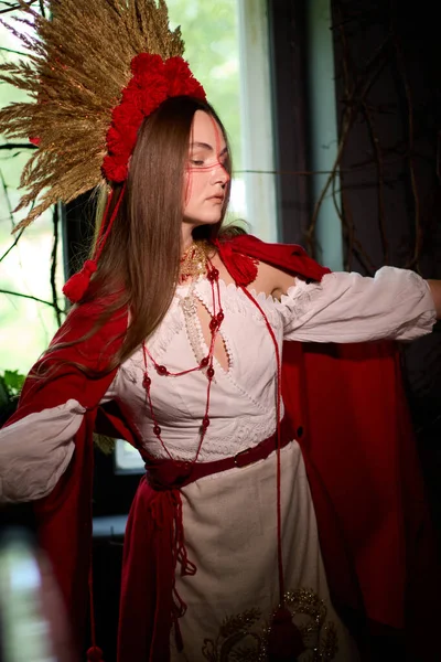 Kırmızı pelerinli, kırmızı başlıklı ve kırmızı ponponlardan yapılmış çarpıcı başlıklı, geleneksel Ukrayna giysileri içinde güzel bir kadının büyüleyici portresi.. 