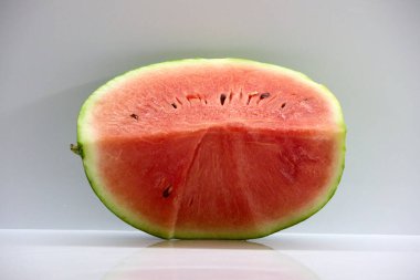 A juicy watermelon cut in half on a white background showcases its vibrant red flesh and black seeds, perfect for summer, refreshment, and healthy eating concepts .